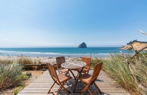A wooden deck with a round table and four chairs overlooking a beach with a prominent rock formation in the distance. - Headlands Coastal Lodge & Spa (Pacific City)