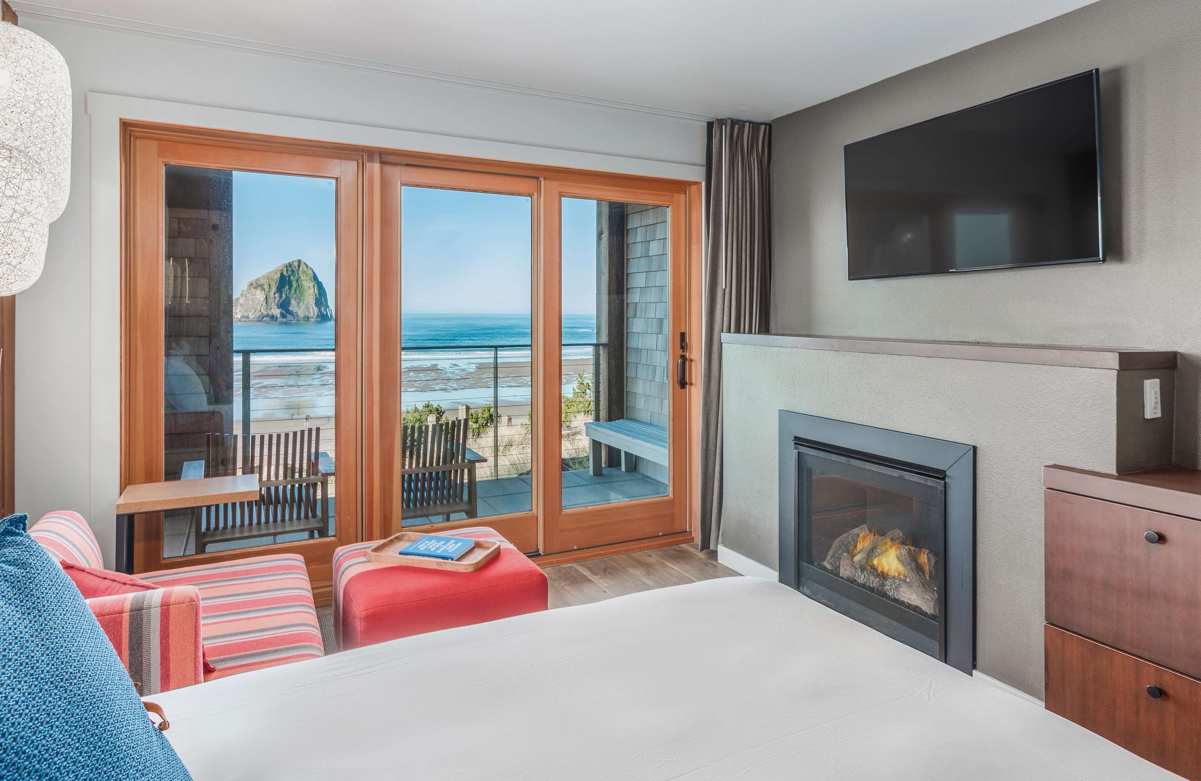 Habitación de hotel con una cama grande, chimenea, televisor y balcón con vista al océano.