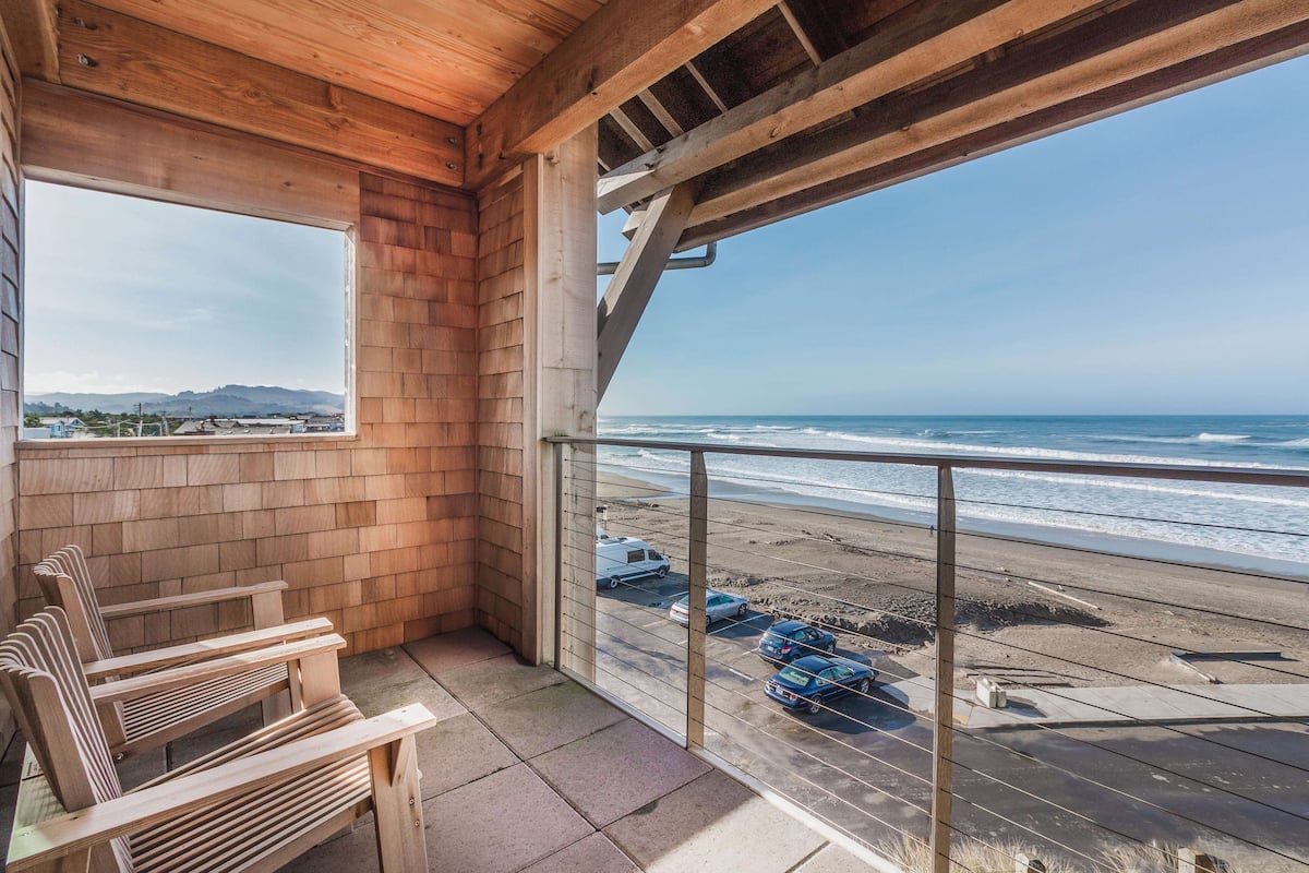 Un balcon en bois offrant une vue sur la plage et les voitures garées.