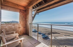 Un balcón de madera con vista a la playa y coches aparcados.