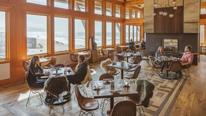 A restaurant with large windows overlooking the ocean, wooden interior, and a fireplace.
