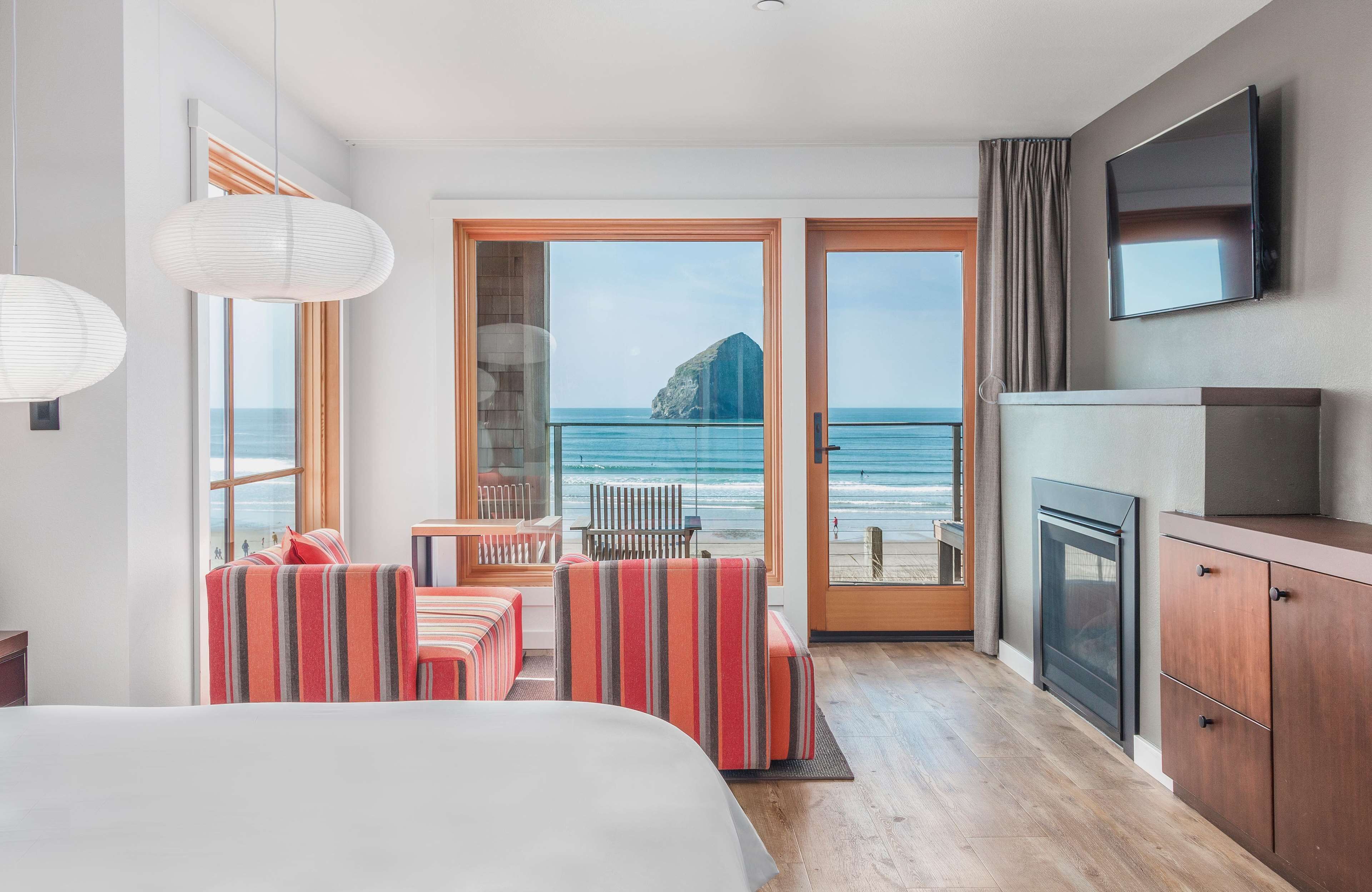 A hotel room with a large bed, a seating area with striped cushions, a television, and a view of the ocean.