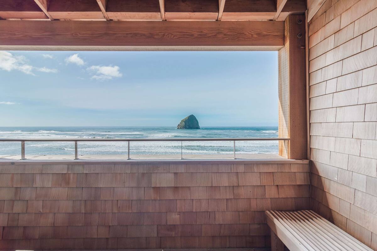 Un balcon en bois offrant une vue sur l’océan et une formation rocheuse.