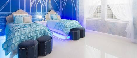 Une chambre à coucher avec un lit, deux poufs, un lustre et une fenêtre ornée de rideaux légers.