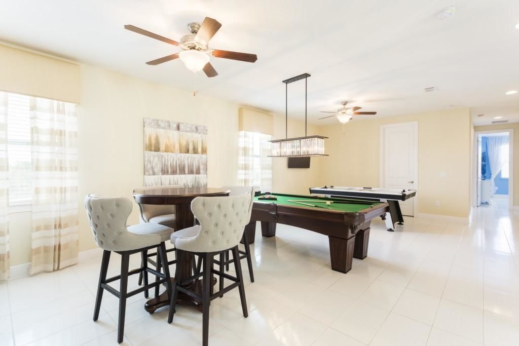 A spacious room with a pool table, two ceiling fans, and a dining area with chairs.
