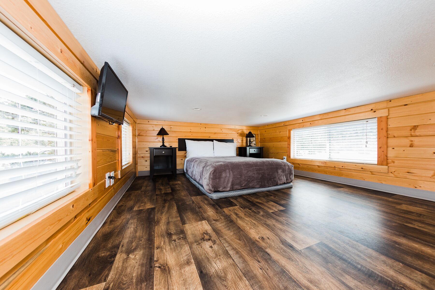 A bedroom with a bed, a nightstand, a lamp, and a TV mounted on the wall.