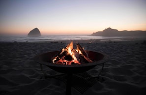 A beach scene with a fire pit in the foreground and a large rock formation in the background. - Hart's Camp (Pacific City)