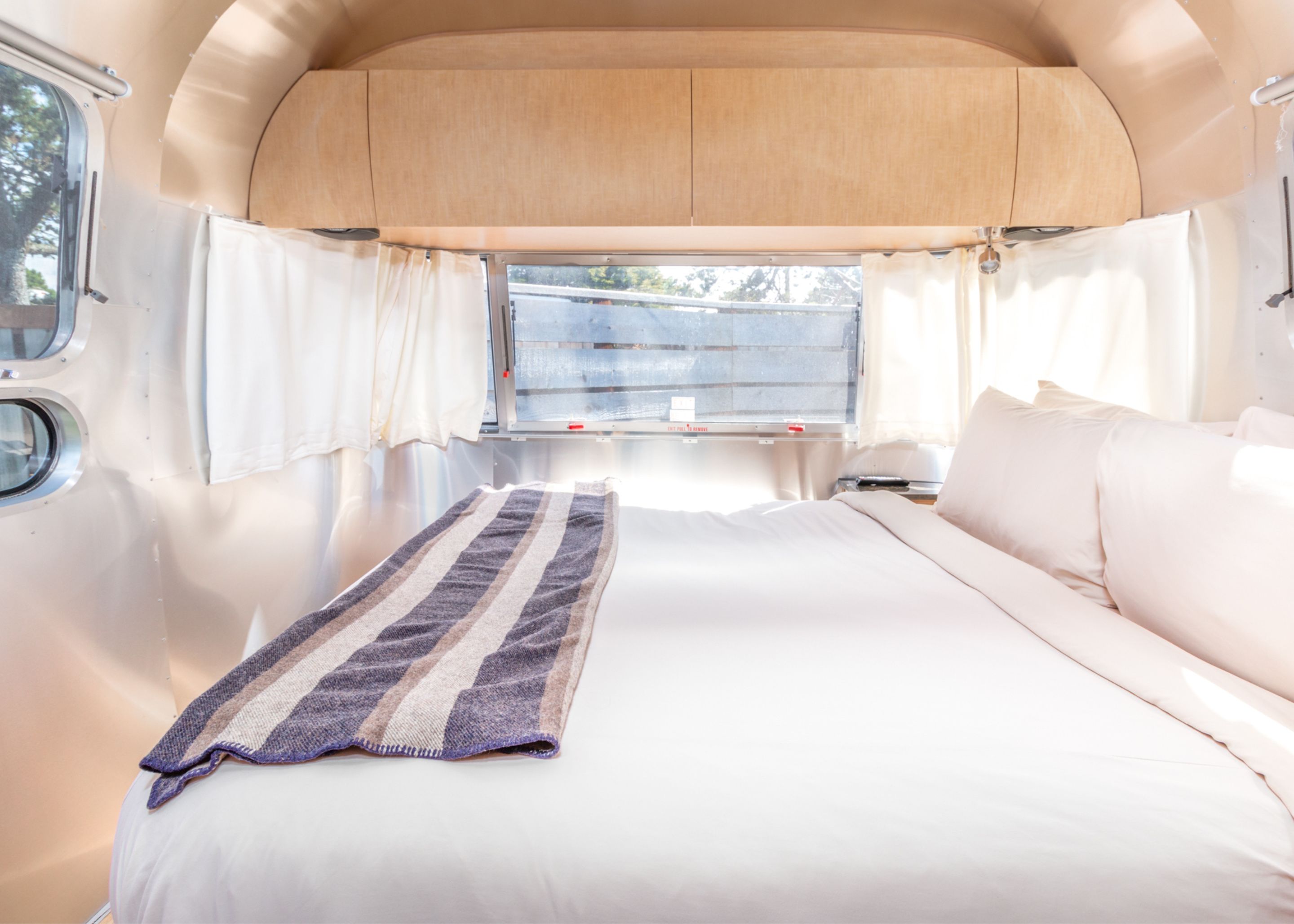 Un intérieur spacieux pour un véhicule récréatif, avec un grand lit, une fenêtre avec des rideaux et un plafond en bois.