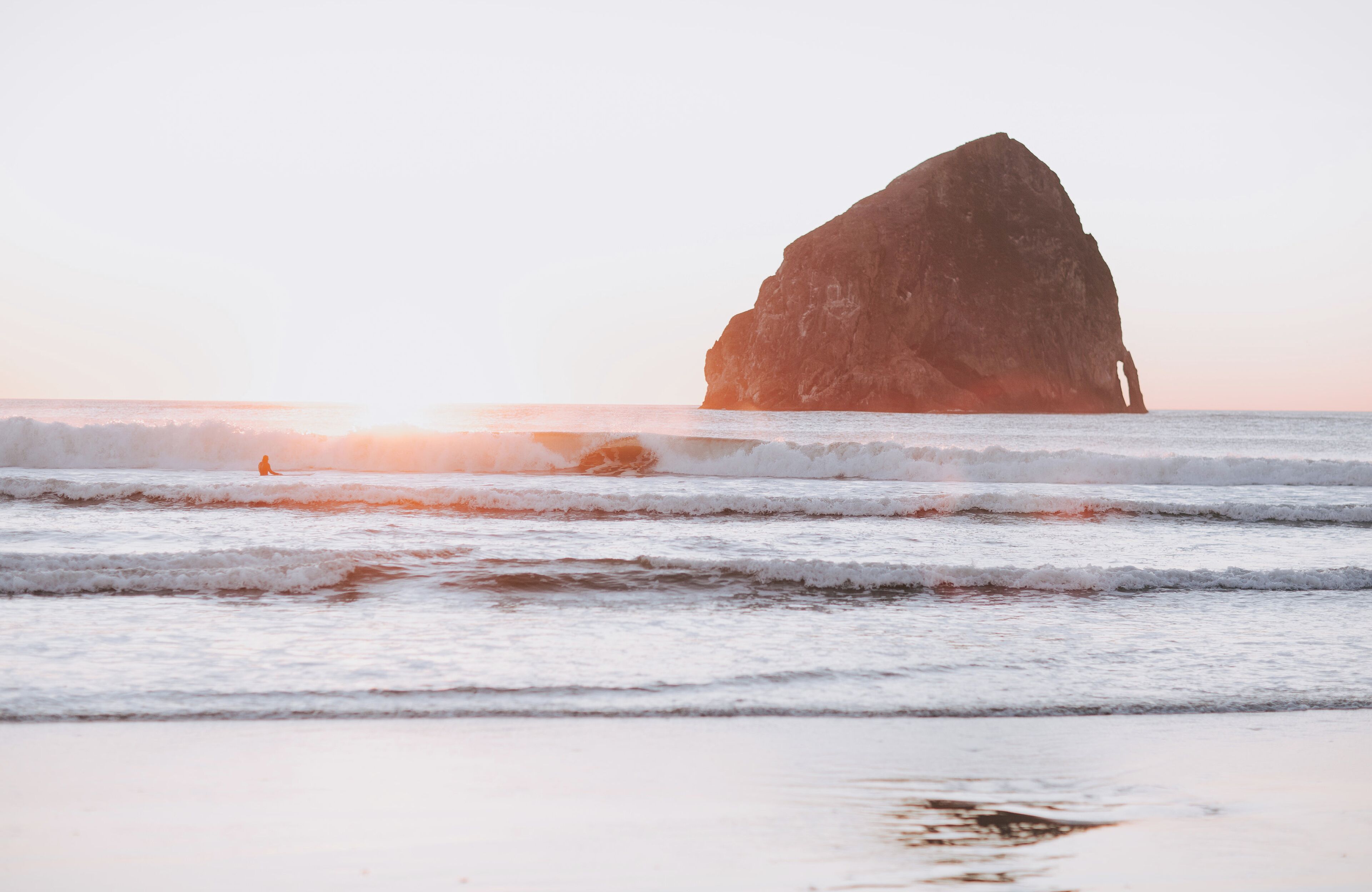 A large rock formation in the ocean with waves approaching the shore.