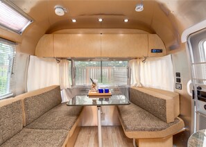 A compact RV interior with a kitchenette, two cushioned seating areas, and a window providing a view of the outdoors.