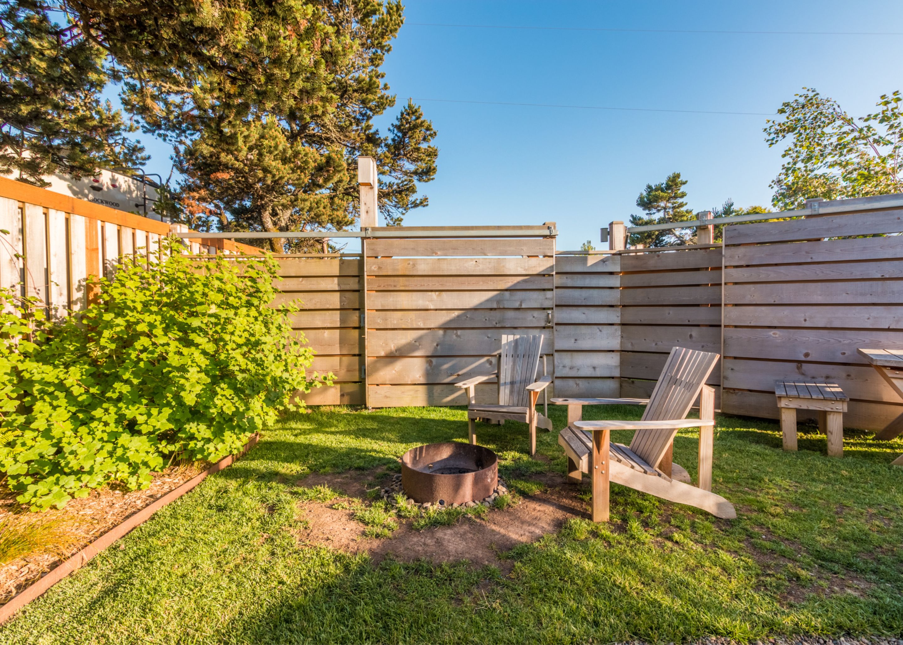 Un jardin avec une clôture en bois, un foyer et deux fauteuils Adirondack.