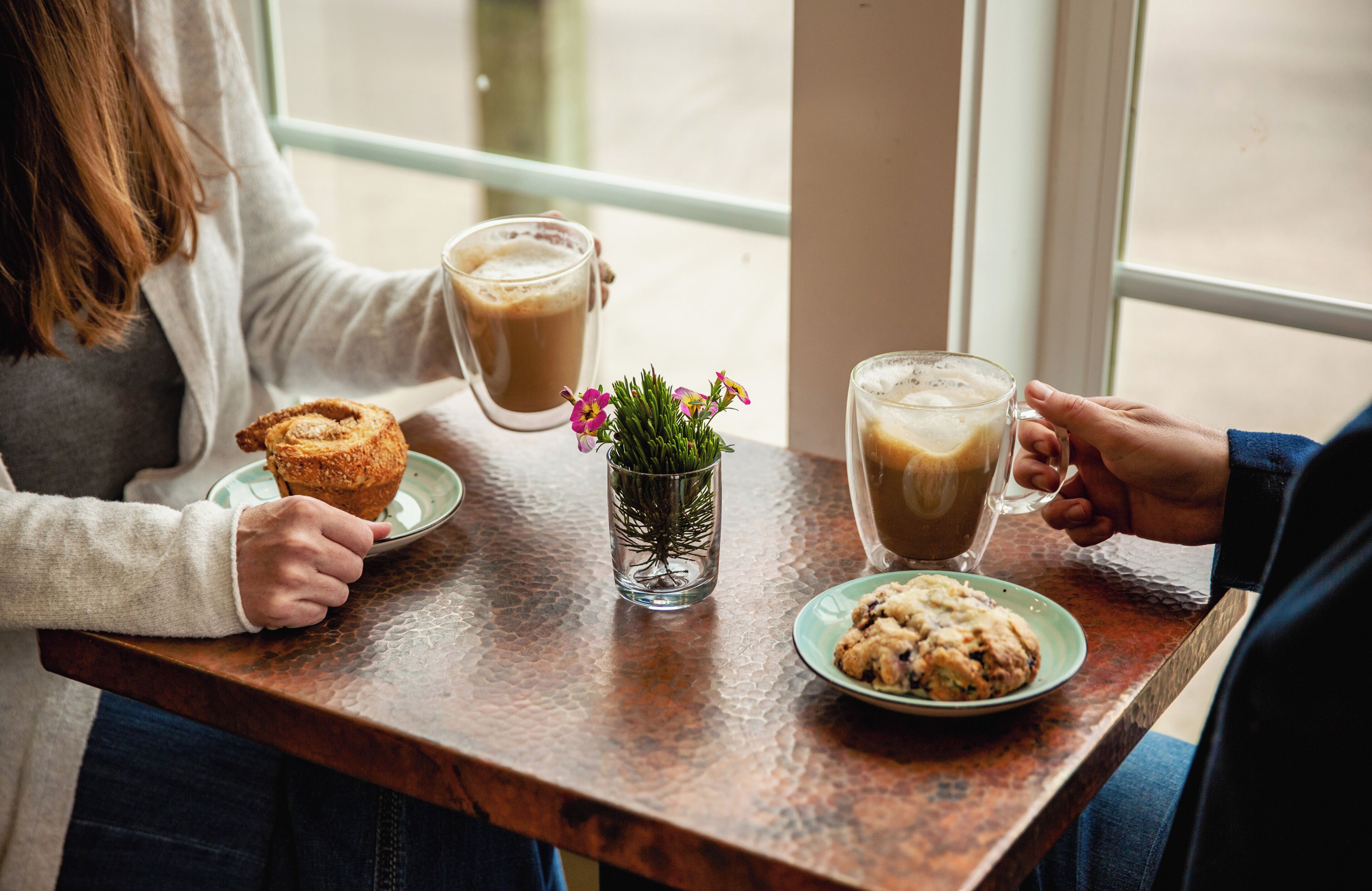 A table with a glass of coffee, a muffin, and a small plant.