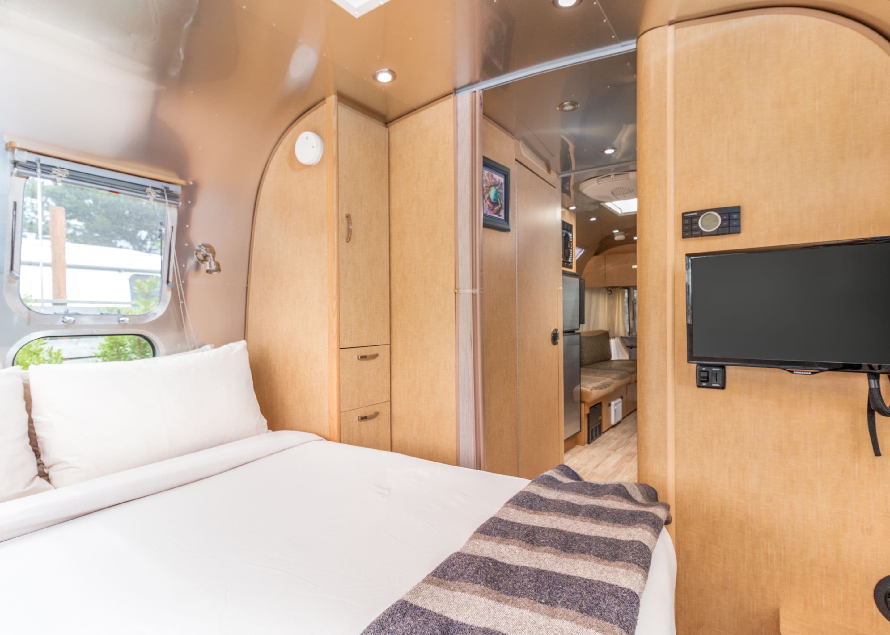 Un intérieur de camping-car compact comprenant un lit, un téléviseur et un coin cuisine.