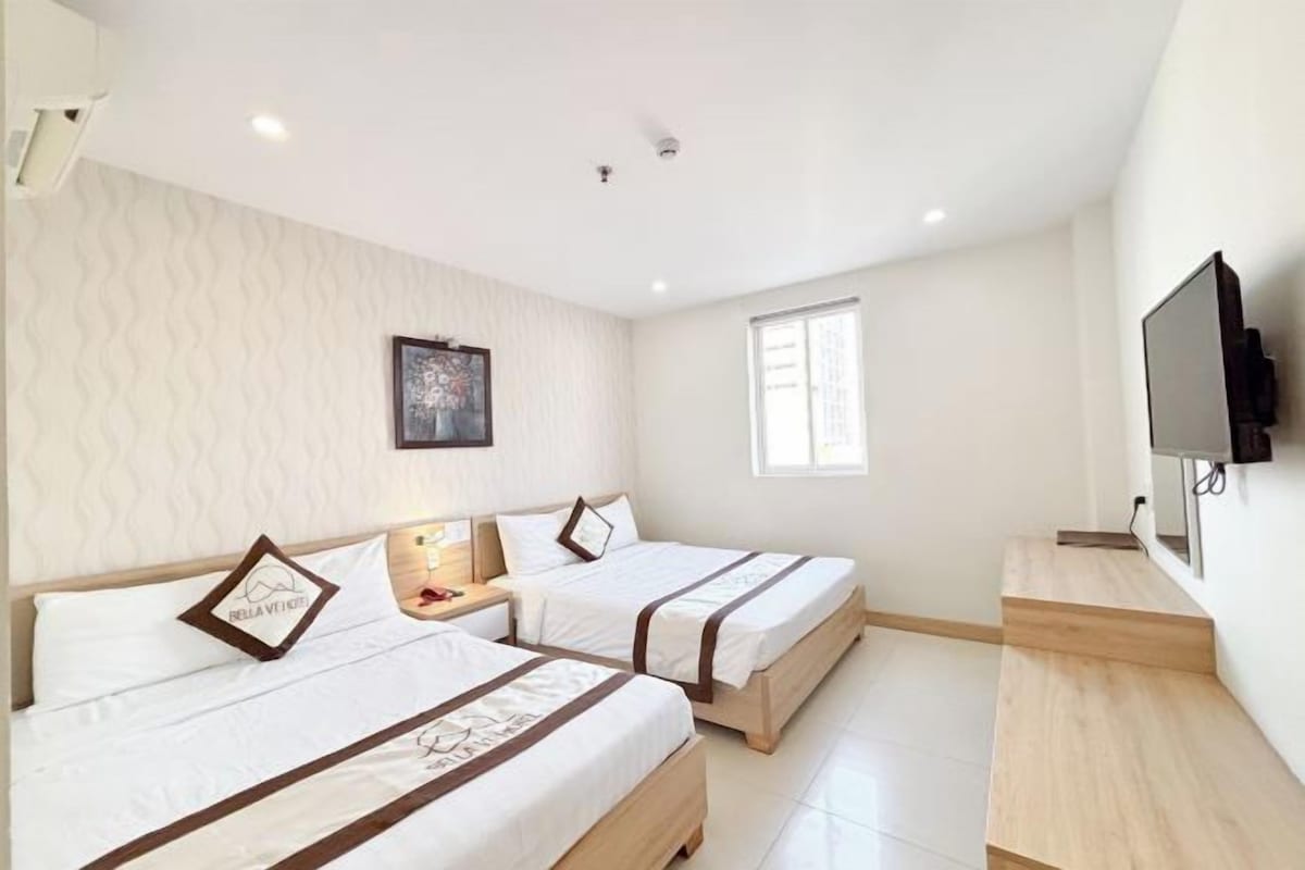 A hotel room with two beds, a TV, a painting on the wall, and a window.