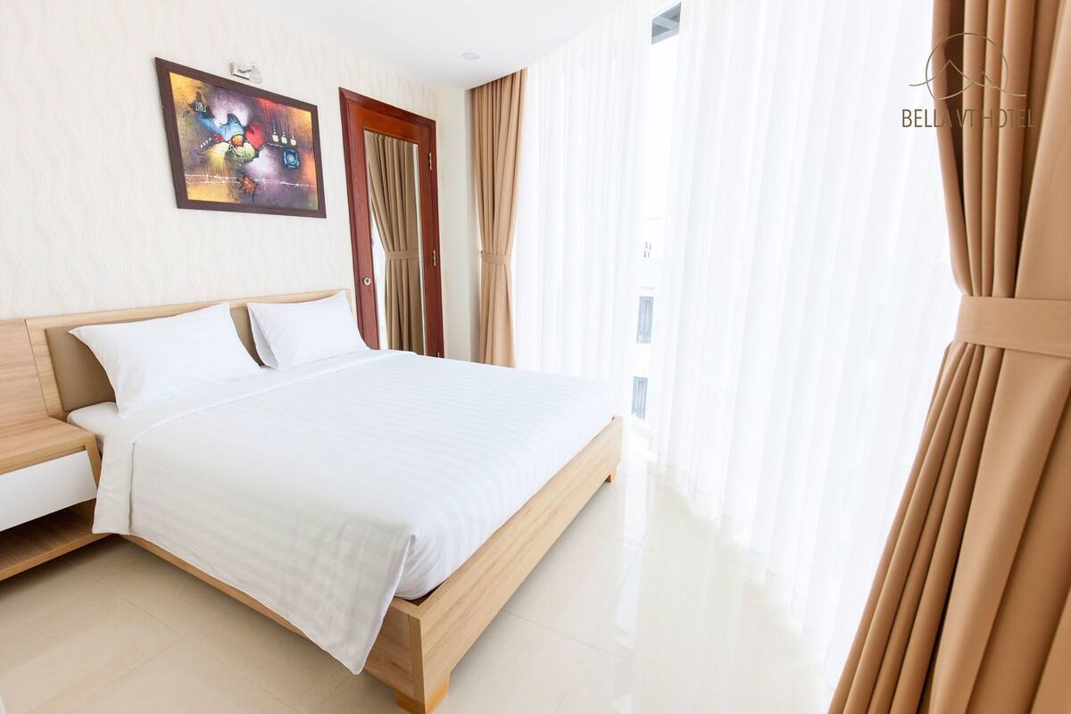 A hotel room with a bed, bedside table, and a painting on the wall.