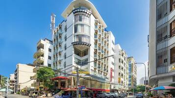 A multi-story hotel with a curved corner design, balconies, and a ground-level commercial area with outdoor seating.