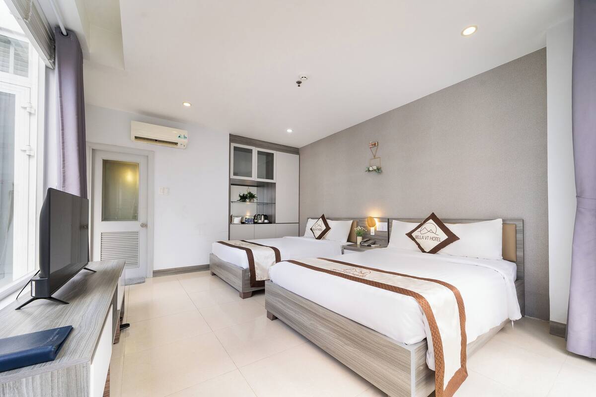A hotel room with two beds, a TV, a desk, and a window.