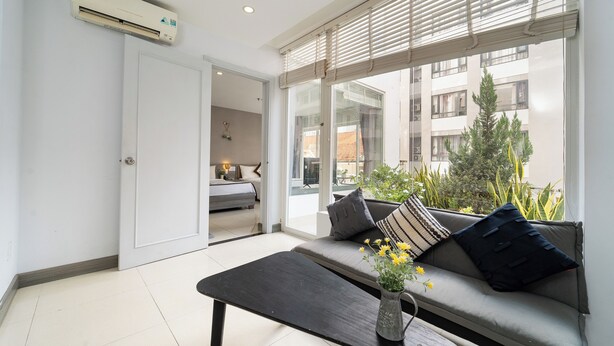 A modern living room with a sofa, a coffee table, and a view of the outside. - Bella VT Hotel - Bai Sau Vung Tau (Ho Chi Minh City)