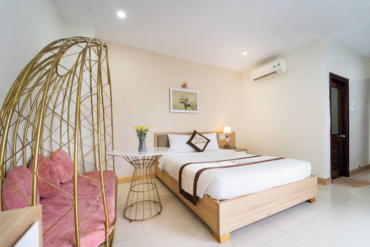 A bedroom with a bed, a hanging chair, a small table, and a wall-mounted air conditioner.
