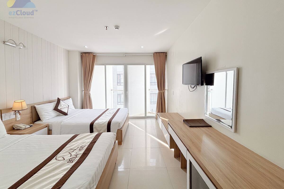 A hotel room with two beds, a desk, a TV, and a balcony with curtains.