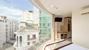 A modern hotel room with a balcony, large windows, and a view of the cityscape. - Bella VT Hotel - Bai Sau Vung Tau (Ho Chi Minh City)