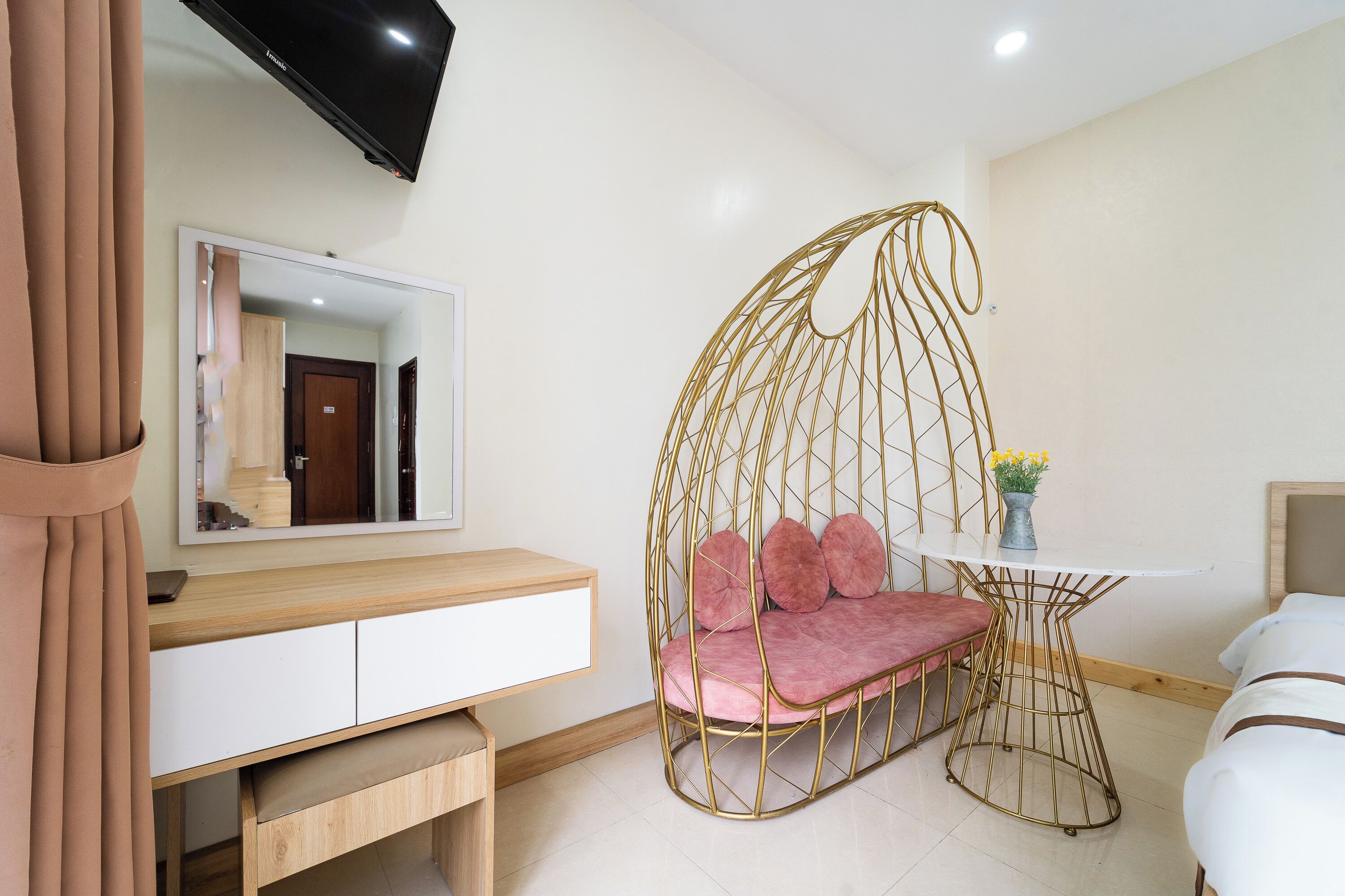 A modern bedroom with a hanging chair, a bedside table, a mirror, and a TV mounted on the wall.