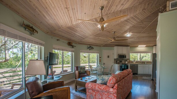 A spacious living area with a wooden ceiling, a red patterned sofa, and a dining table. - Indian Pass Fun,  Private & Cozy Beach Cottage--The Barnacle (Port St Joe)