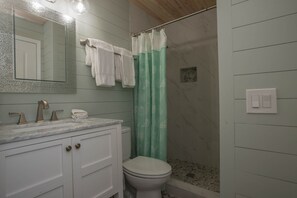 Une salle de bain avec un lavabo en marbre, des meubles blancs, des toilettes et une douche avec un rideau vert.
