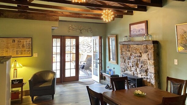 A dining area with a stone fireplace, wooden ceiling beams, and a view through glass doors to an outdoor patio. - 1 bedroom with SPA bathroom and mountainside deck  (Jim Thorpe)