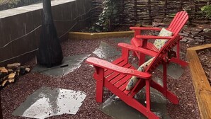 A patio with red Adirondack chairs, a black vase, and a small wooden structure with windows. - 1 bedroom with SPA bathroom and mountainside deck  (Jim Thorpe)