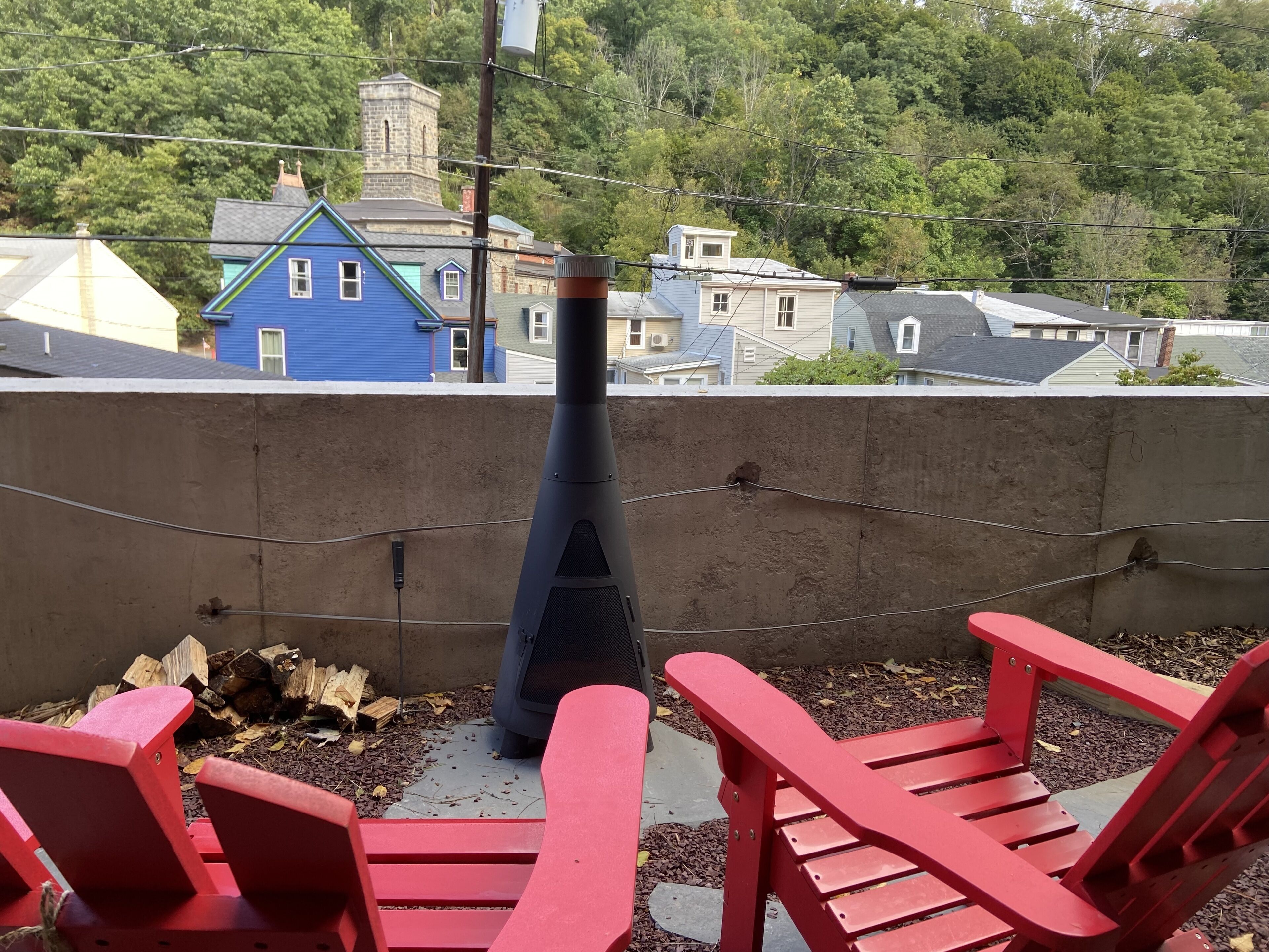 Un balcon avec des fauteuils Adirondack rouges, un mur en béton et une vue sur des maisons et des arbres.