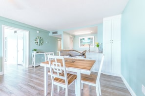 Un comedor con una mesa de madera y sillas blancas, una escultura de pez y vistas a la cocina.