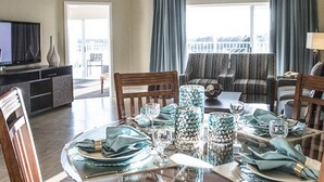 Comedor con una mesa redonda dispuesta para cuatro personas, un ventilador de techo y un televisor sobre un mueble.