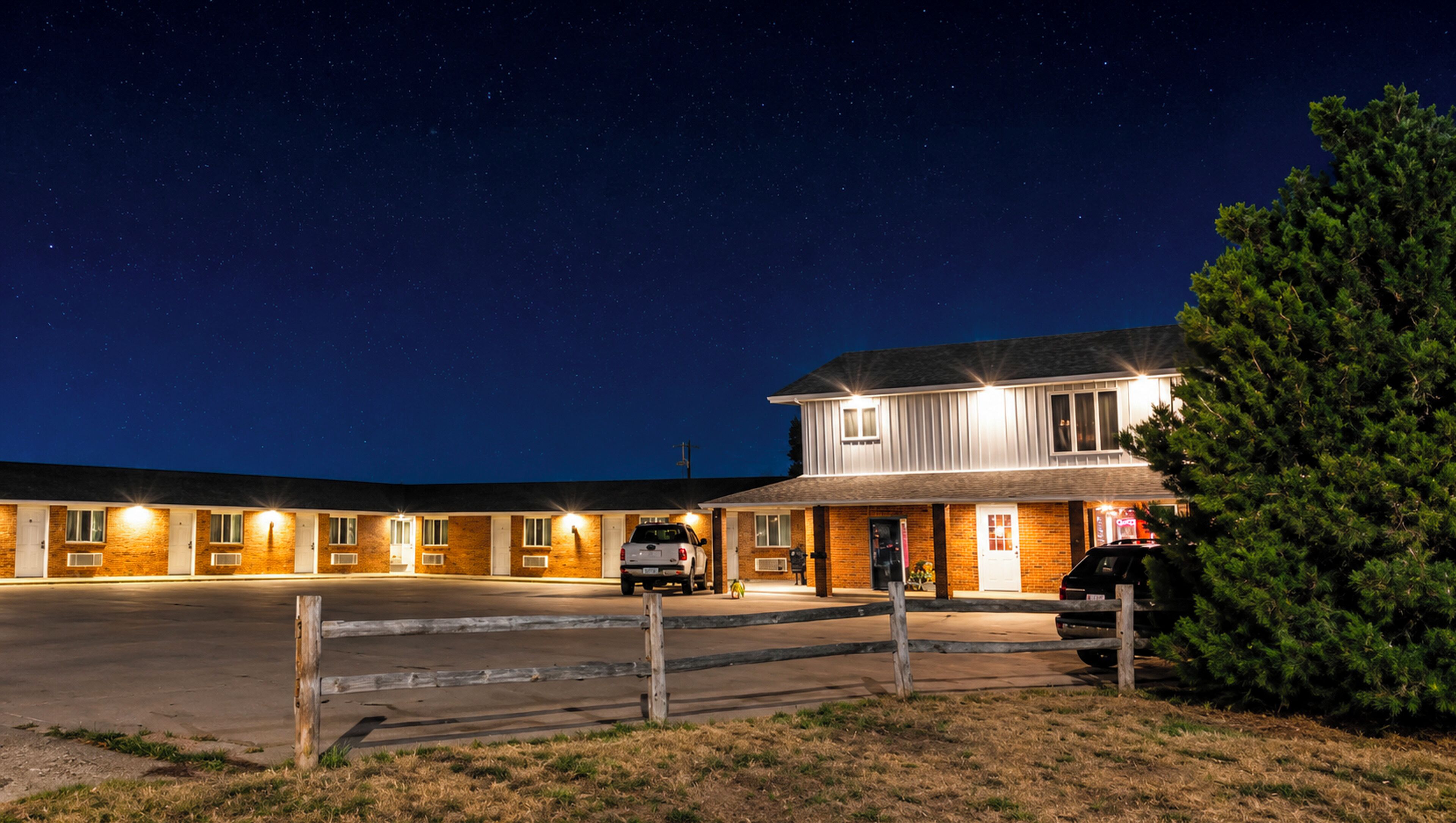 A motel with multiple rooms, a parking area, and a large tree in the foreground.