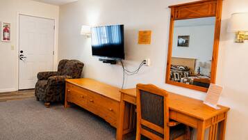 A hotel room with a wooden desk, a television, a chair, a dresser, a mirror, and a door.
