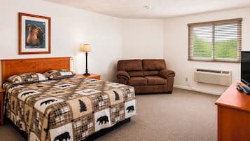 A bedroom with a bed, a brown leather chair, a bedside table with a lamp, a wall-mounted TV, and a window with blinds.