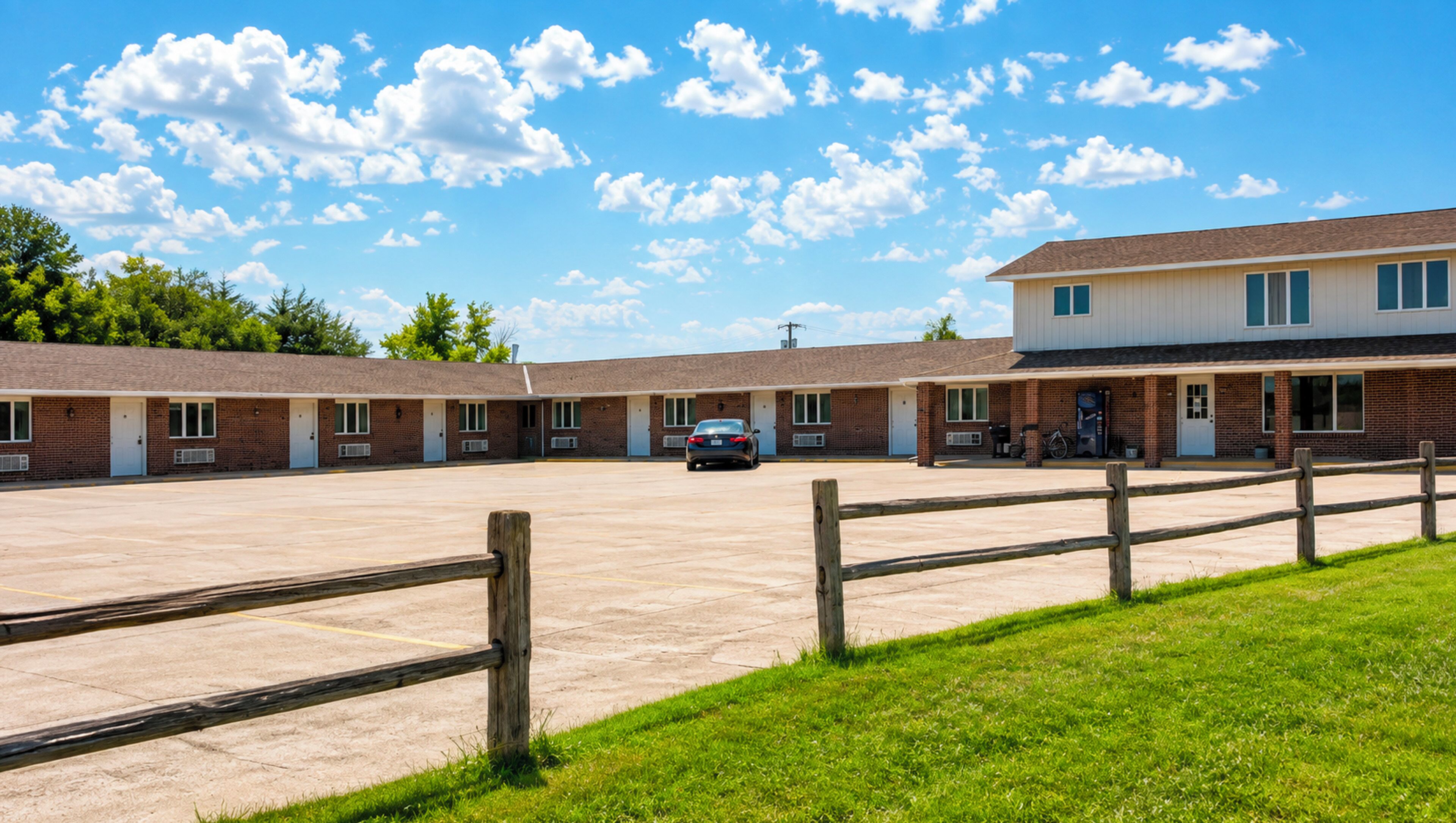 A motel with a parking lot, a car, and a grassy area.