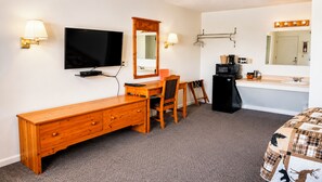 A hotel room with a wooden dresser, a desk with a chair, a television, a mirror, a refrigerator, a sink, and a bed with a plaid bedspread. - Drop Tyne Lodge (Franklin)