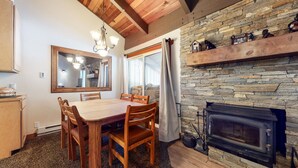 Un comedor acogedor con una mesa y sillas de madera, una chimenea de piedra y un espejo grande sobre la mesa.