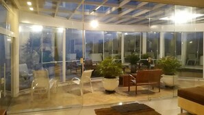 Ein modernes Wohnzimmer mit Glaswänden, einer Holzbank und Topfpflanzen.