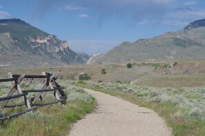 Un chemin de gravier traverse une région montagneuse, avec une clôture en bois sur le côté gauche.