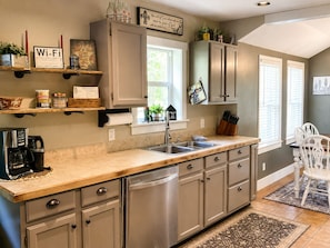 A kitchen with a dishwasher, a coffee maker, and a sink. There are cabinets, a window, and a plant on the counter. - “The Wyoming,” A Beautiful historic downtown home. (Cody)