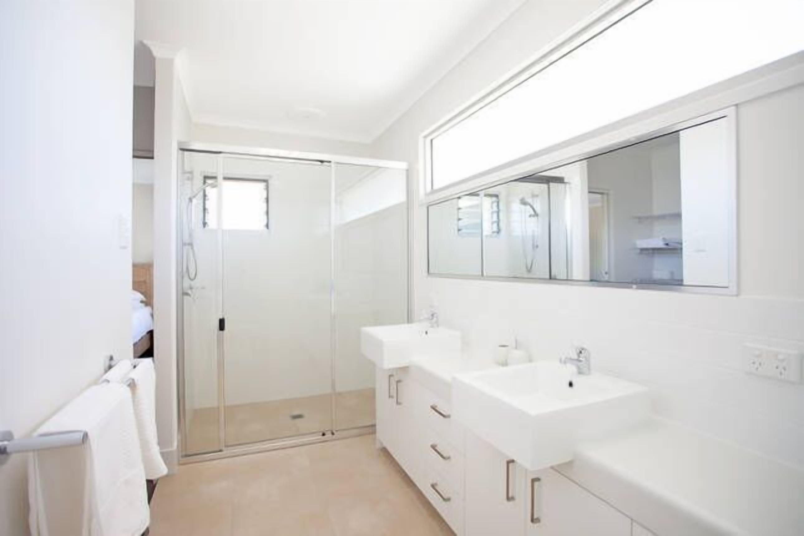 Une salle de bain moderne avec une douche à l’italienne en verre, deux vasques et un grand miroir.