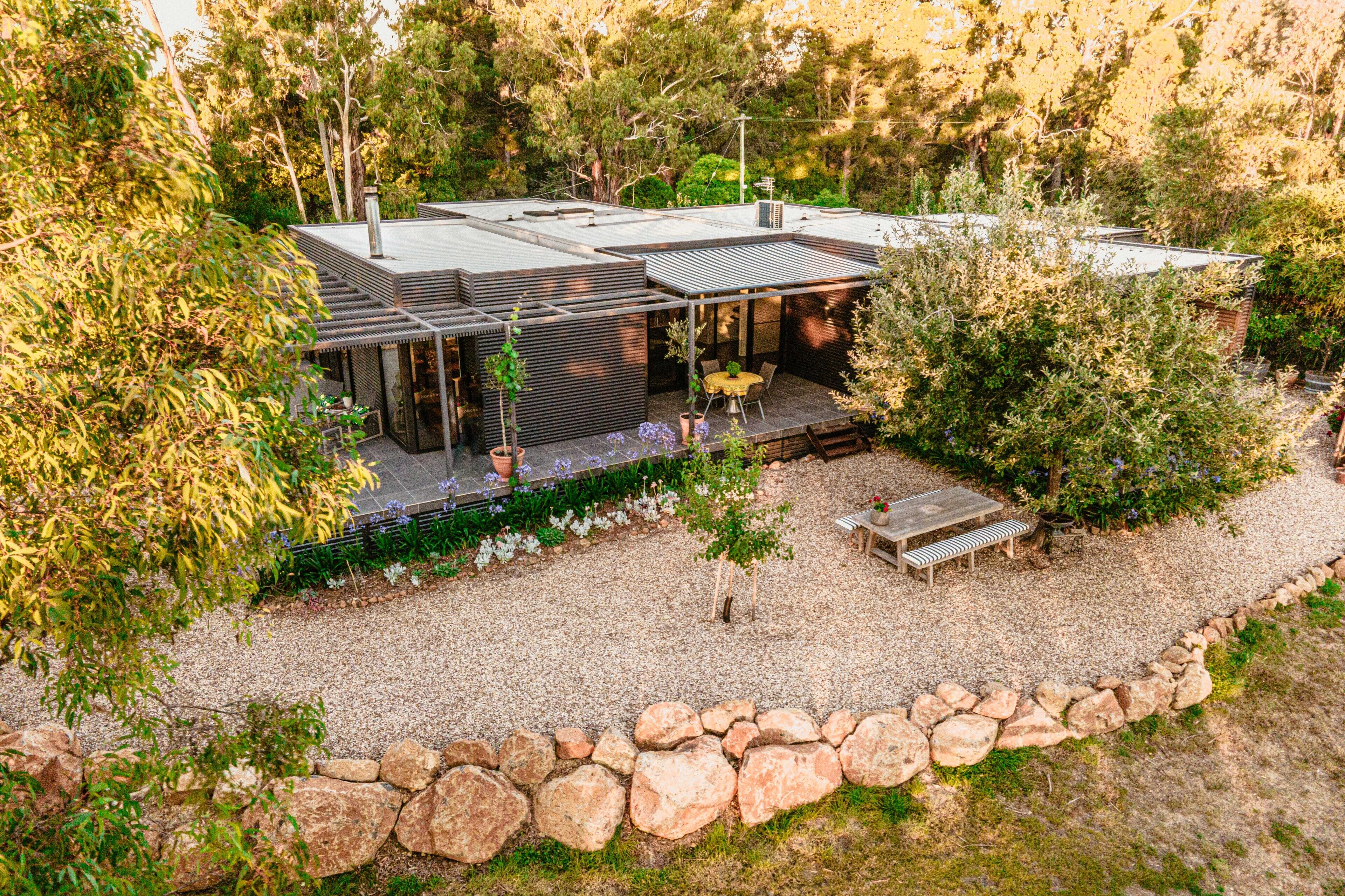 Una casa moderna con patio, mobiliario exterior y un muro de piedra.