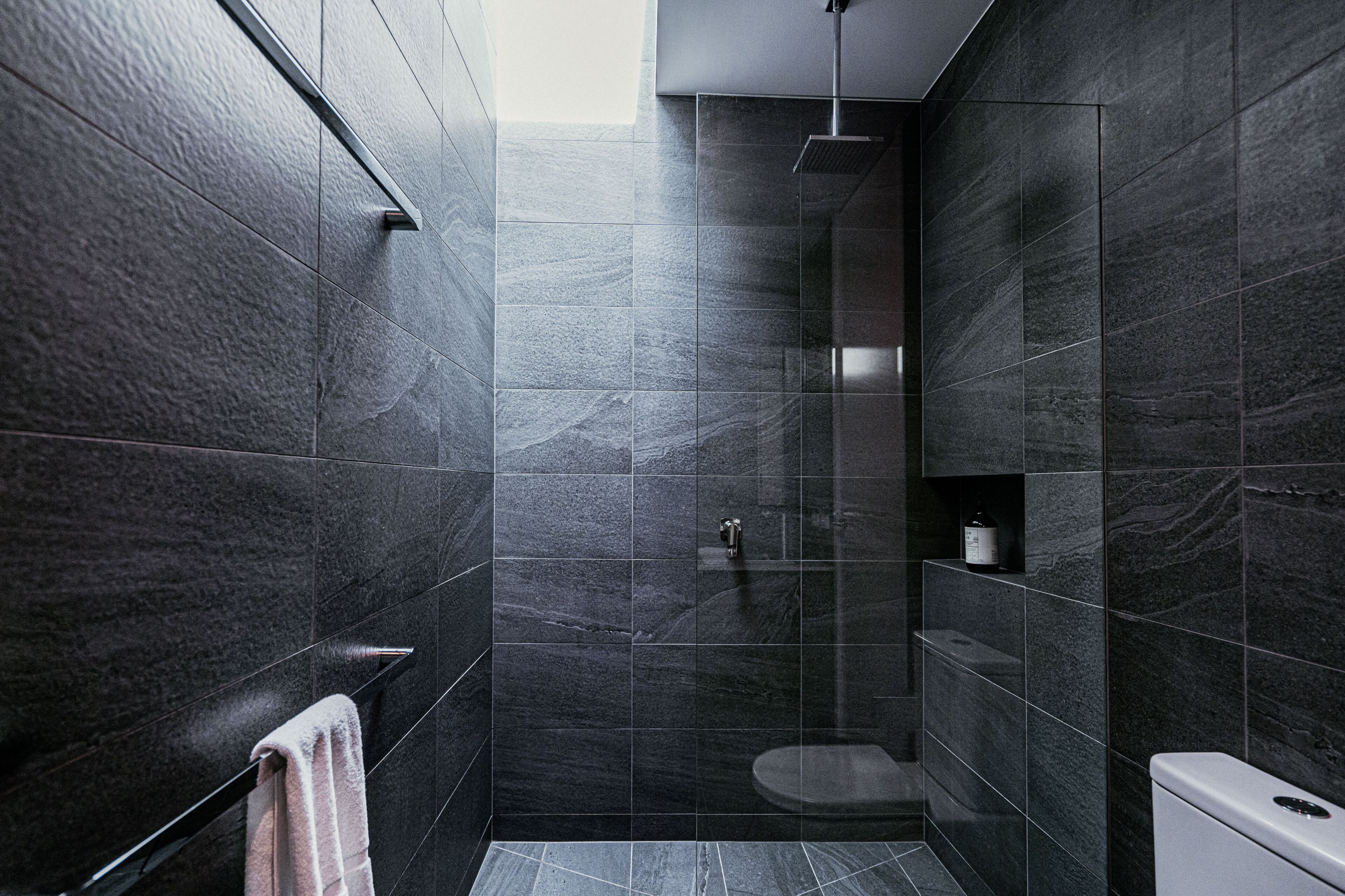 Une salle de bain moderne avec des carreaux de couleur sombre, une douche en verre, des toilettes et un porte-serviettes.