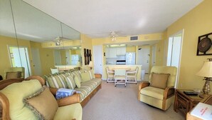 A living room with a sofa, chairs, a dining table, and a kitchen area in the background. - Beachfront 1BR condo with heated pool, kitchen, WiFi, and king bed. (Marco Island)