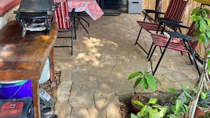 Eine Terrass mit Steinbelag, einem Grill, einem Tisch und Stühlen. Es gibt Blumentöpfe und ein Wandgemälde.