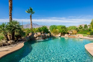 A clear blue pool with a waterfall feature, surrounded by palm trees and rocks.