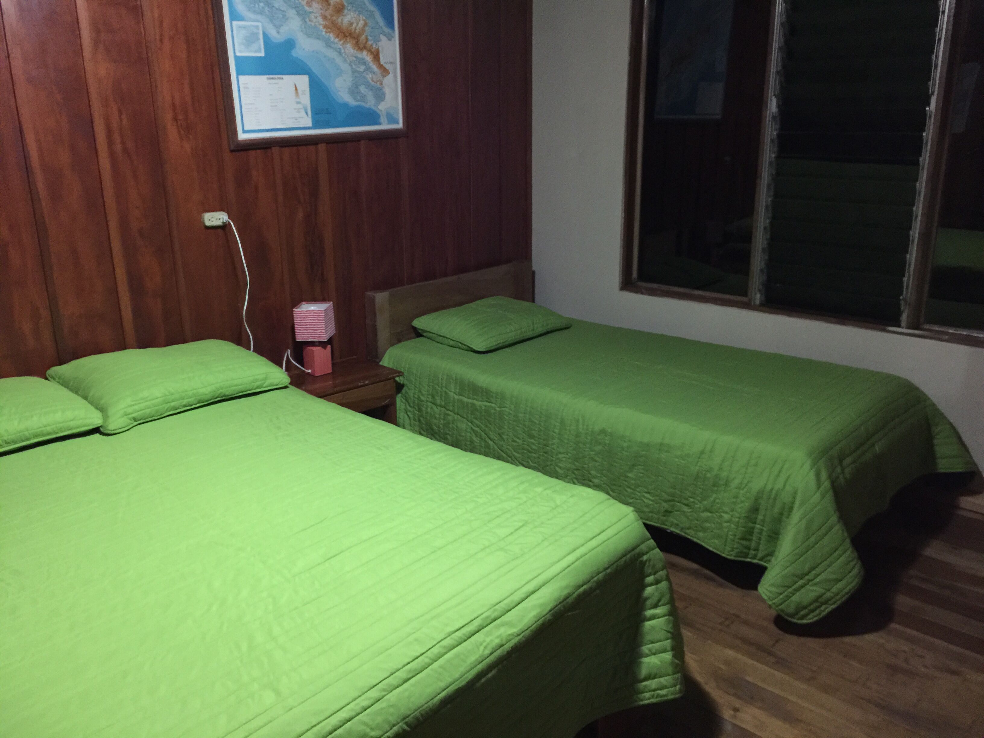 Une chambre avec deux lits, des murs en bois, une carte accrochée au mur et une fenêtre.