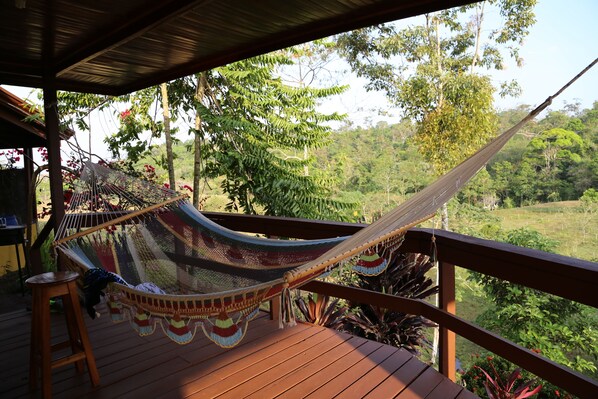 Un hamac sur une terrasse en bois, avec vue sur un paysage boisé.